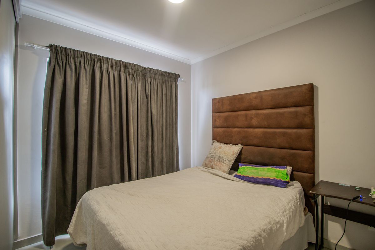 A well-maintained bedroom featuring neutral wall finishes, cove cornicing, and a functional curtain track system.