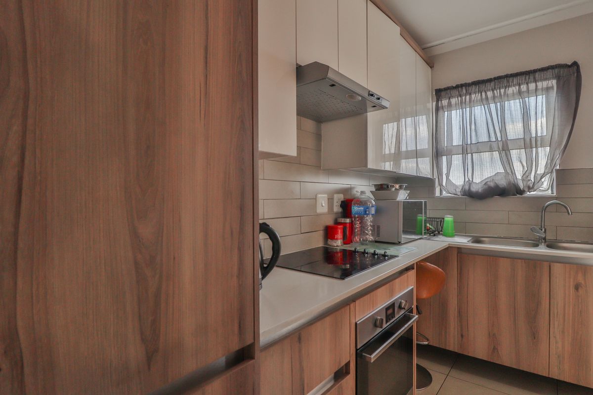 Modern kitchen featuring wood-grain cabinetry, stone countertops, a built-in oven, electric hob, and a stainless steel sink with a tiled backsplash.