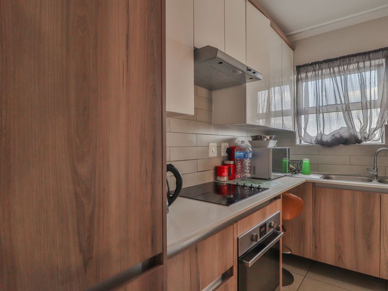 Modern kitchen featuring wood-grain cabinetry, stone countertops, a built-in oven, electric hob, and a stainless steel sink with a tiled backsplash.