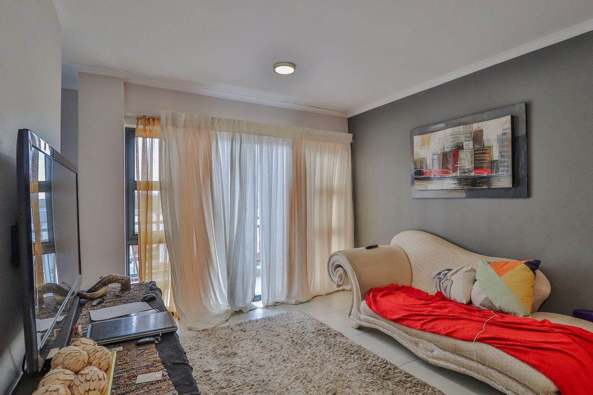 A comfortable living room featuring tiled flooring, a sliding glass door providing natural light, and a neutral grey accent wall.
