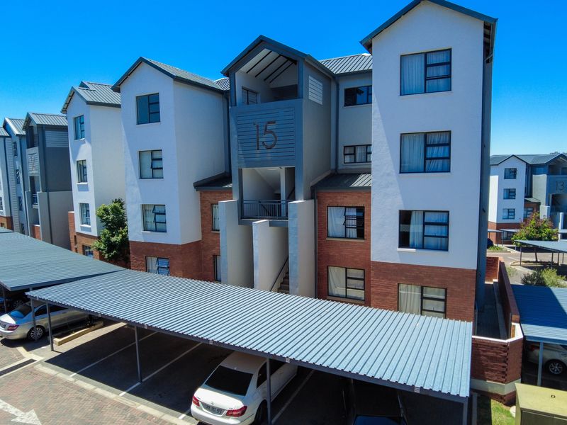 Exterior view of a modern multi-story apartment complex featuring brick and plaster facade, metal roofing, and covered parking bays.