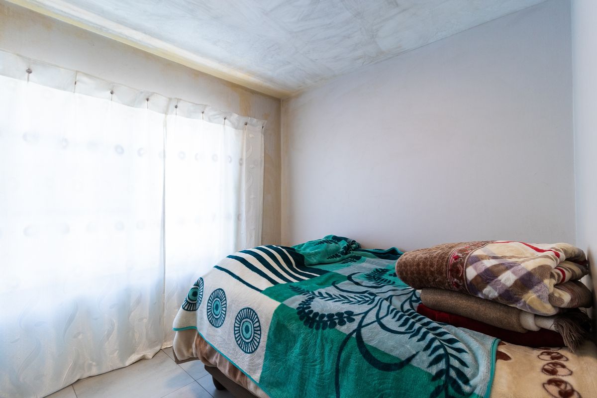 A bedroom featuring tiled flooring, currently showing visible signs of water damage on the ceiling and walls.
