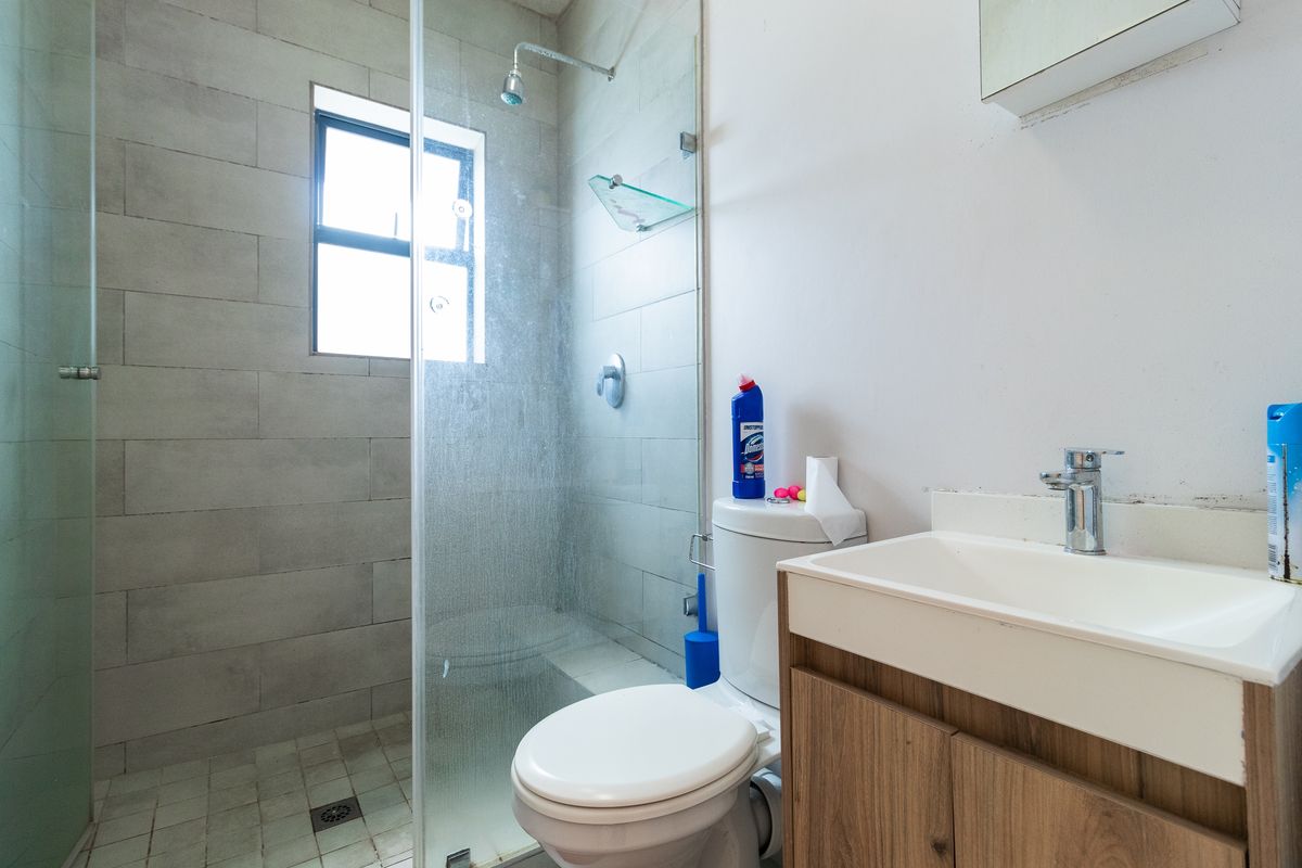 A functional bathroom featuring a glass-enclosed shower, a modern vanity with basin, and a standard toilet, finished with neutral wall tiling.