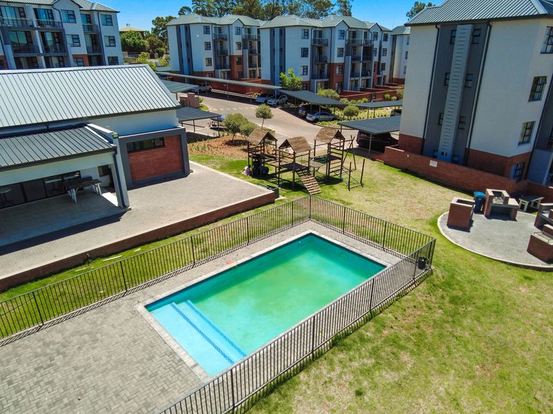 Aerial view of the apartment complex communal area featuring a swimming pool, paved patio, built-in braai facilities, and a children's playground.