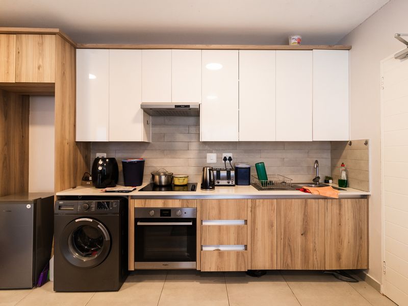 Modern kitchen featuring white and wood-grain cabinetry, built-in oven, electric hob, extractor fan, and tiled backsplash with integrated laundry appliance space.