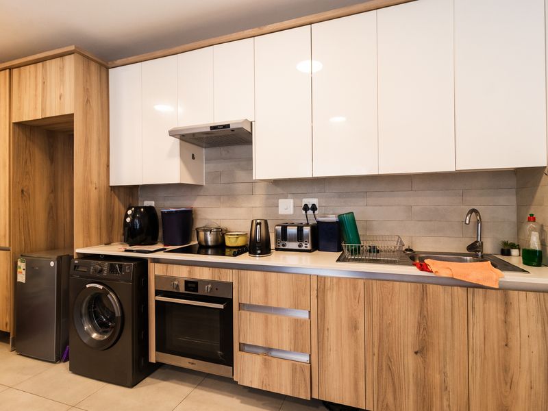 Modern kitchen featuring wood-grain and white cabinetry, integrated oven and hob, tiled backsplash, and durable tiled flooring.