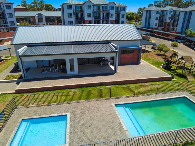 Aerial view of a communal apartment complex pool area featuring two swimming pools, paved decking, and a covered patio structure.