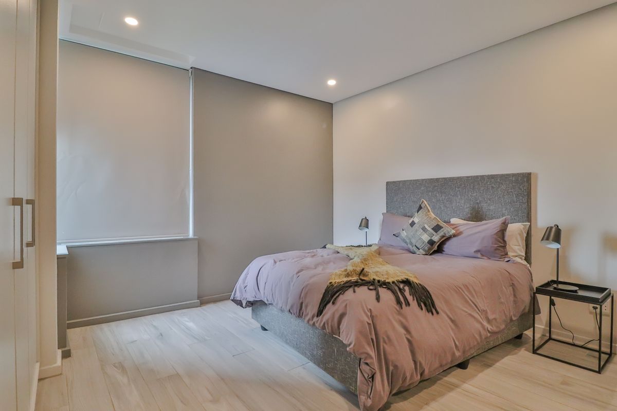 A modern, well-maintained bedroom featuring light laminate flooring, recessed downlighting, and a built-in wardrobe with neutral wall finishes.