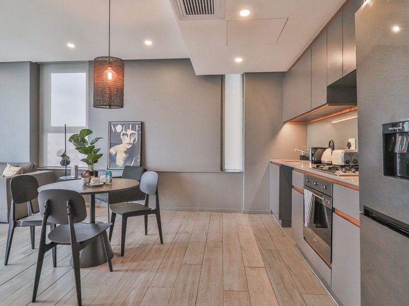 Modern open-plan living and kitchen area featuring sleek grey cabinetry, integrated appliances, recessed lighting, and durable timber-look flooring.