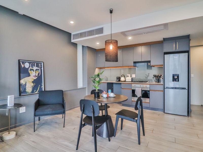 Modern open-plan kitchen and dining area featuring sleek grey cabinetry, integrated appliances, ducted air conditioning, and light wood-look laminate flooring.