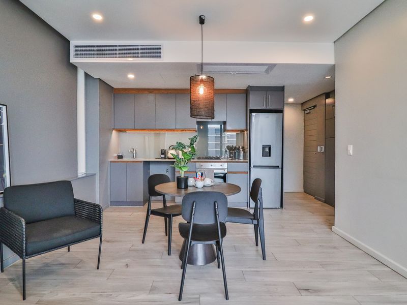 Modern open-plan living area featuring a sleek kitchen with built-in cabinetry, integrated appliances, and ducted air conditioning, finished with contemporary light wood-look flooring.