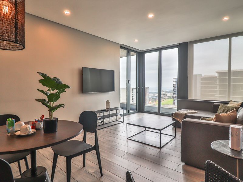 Modern open-plan living and dining area featuring wood-look tile flooring, recessed lighting, and floor-to-ceiling windows with access to a balcony.