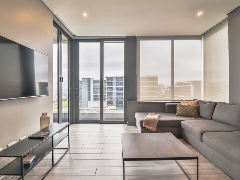 Modern living room featuring large format floor tiles, recessed lighting, and expansive floor-to-ceiling windows with access to a balcony.