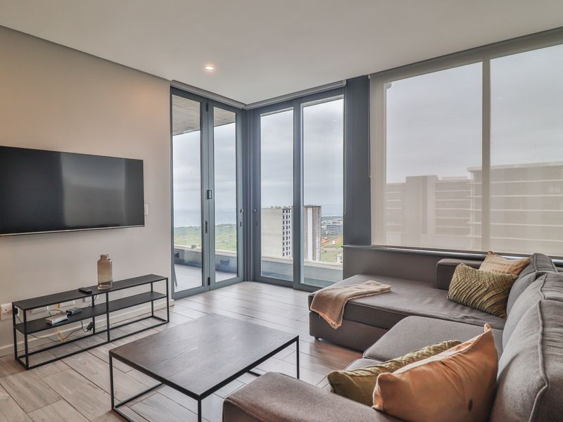 Modern living room featuring large format floor tiles, recessed lighting, and expansive floor-to-ceiling windows with access to a balcony and scenic views.