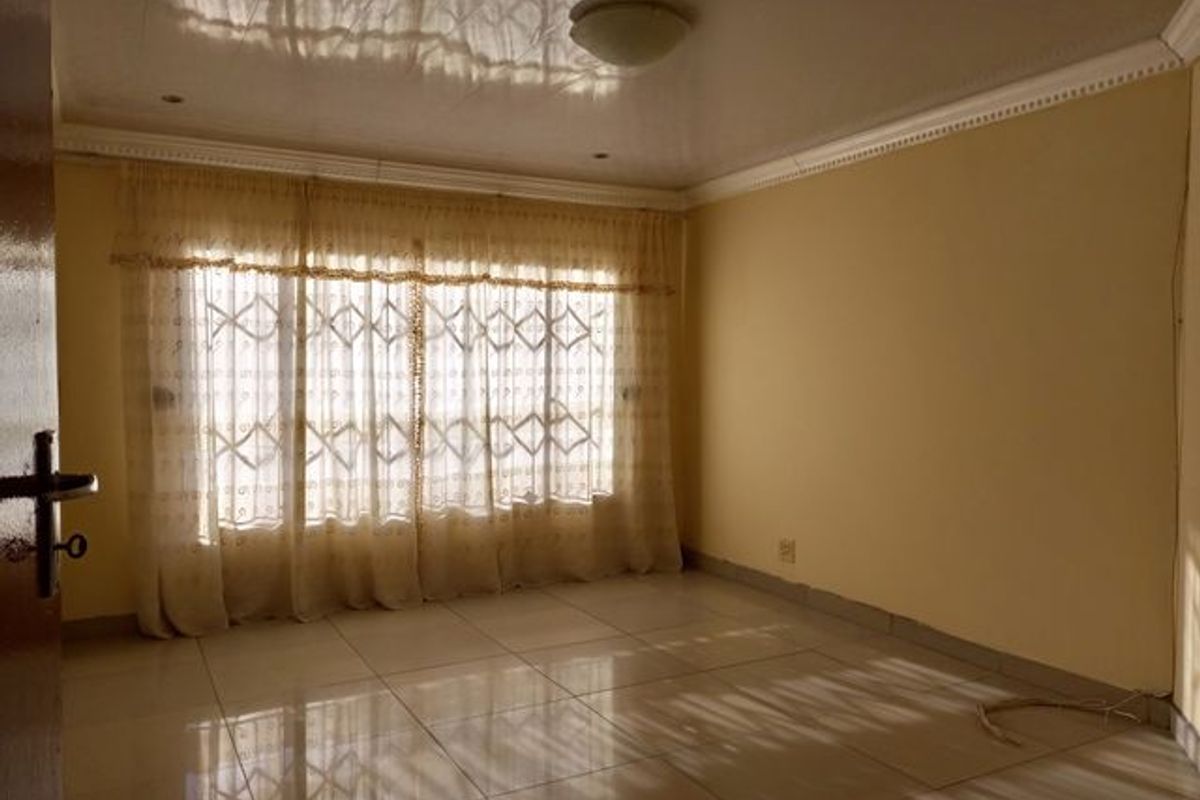 A vacant living room featuring tiled flooring, decorative ceiling cornices, and a large window with security gate.
