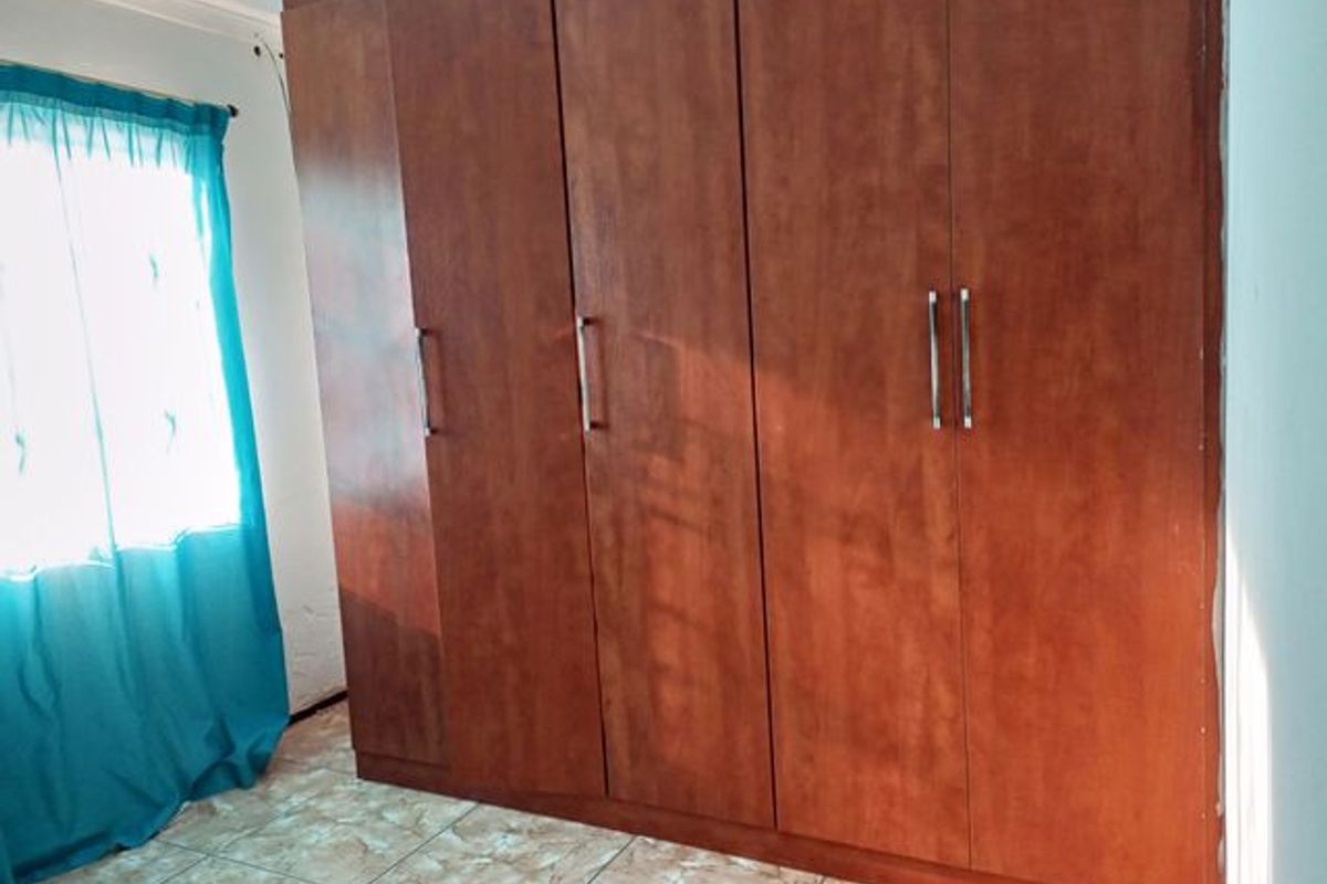 A bedroom featuring built-in wooden wardrobes with metal handles and tiled flooring.