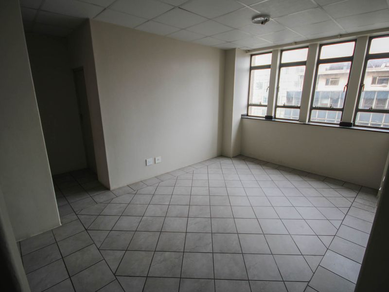 An empty bedroom featuring tiled flooring, a drop ceiling, and large windows providing natural light and urban views.