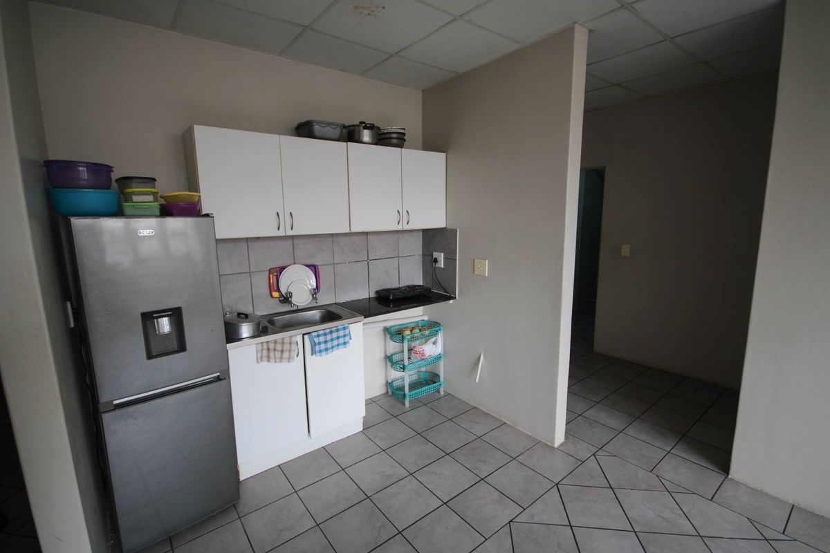 A compact kitchen area featuring white cabinetry, a stainless steel sink, tiled backsplash, and tiled flooring, requiring some cosmetic updates.
