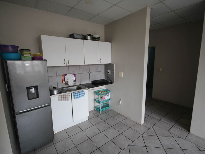 A compact kitchen area featuring white cabinetry, a stainless steel sink, tiled backsplash, and tiled flooring, requiring some cosmetic updates.