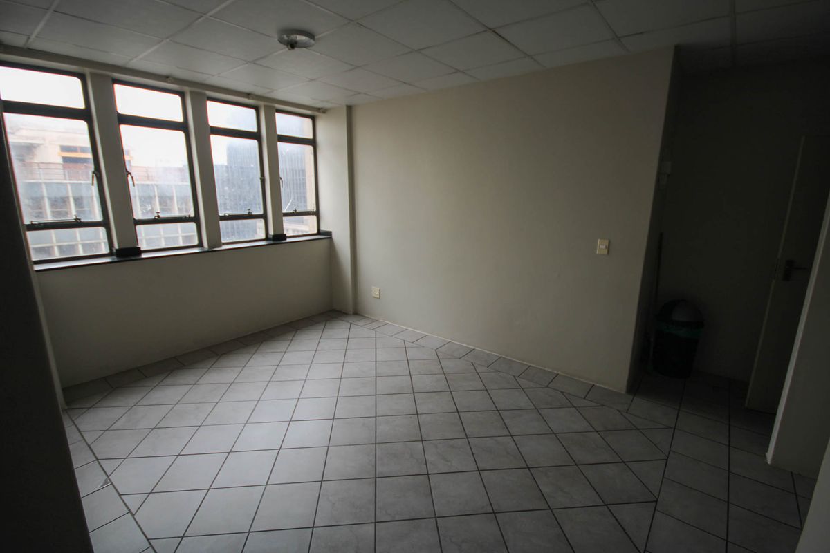 An empty bedroom featuring tiled flooring, a drop ceiling, and large windows providing natural light. The space is ready for renovation or staging.