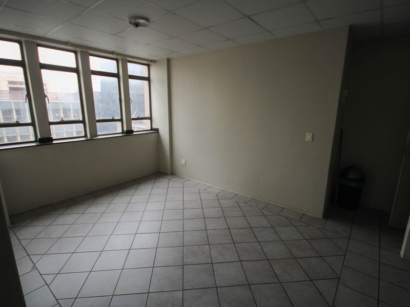 An empty bedroom featuring tiled flooring, a drop ceiling, and large windows providing natural light. The space is ready for renovation or staging.