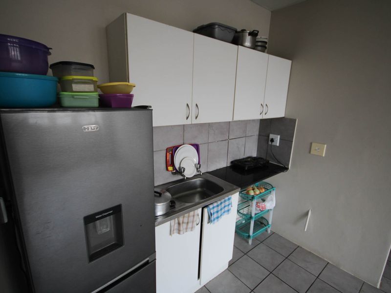A compact kitchen area featuring basic white cabinetry, a stainless steel sink, tiled backsplash, and tiled flooring.