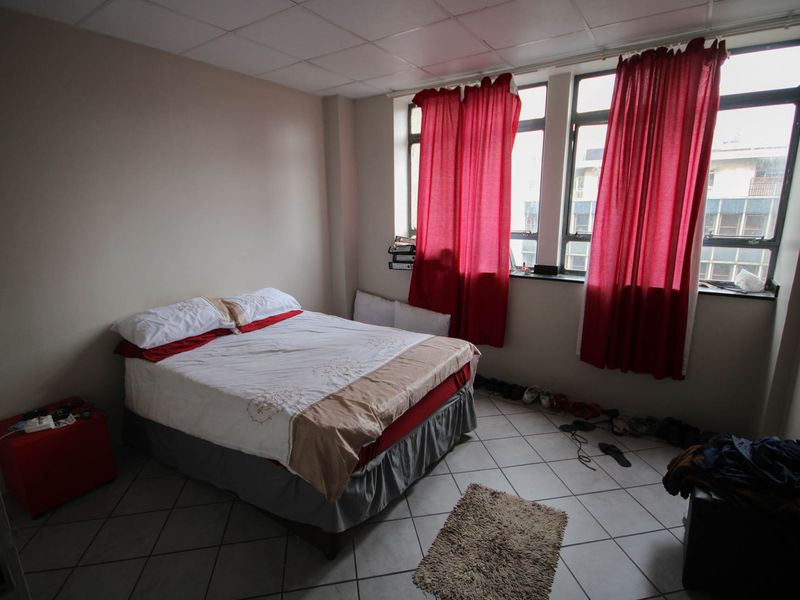 A bedroom featuring tiled flooring and large windows, currently requiring cosmetic updates to the ceiling and overall finishes.