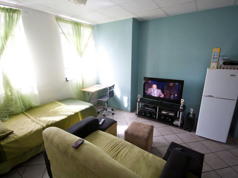 A multi-purpose living and sleeping area featuring tiled flooring and a drop ceiling, suitable for a studio apartment layout.