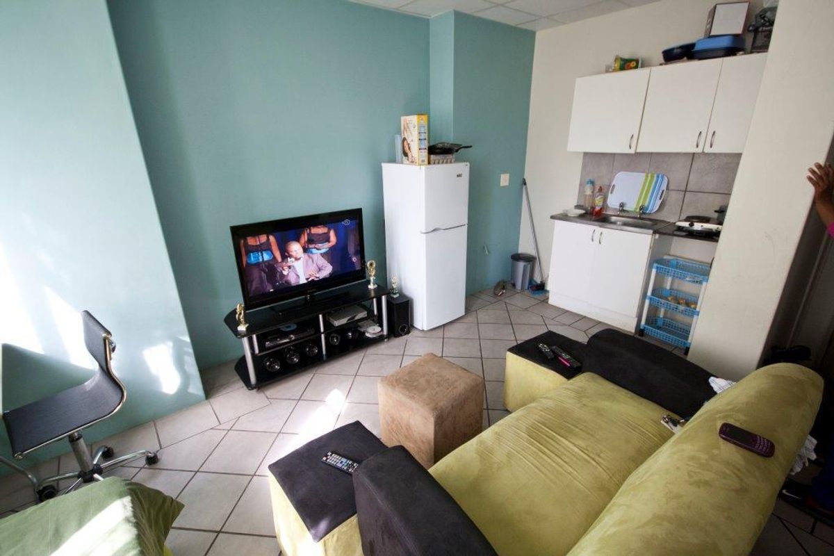 Compact open-plan living area featuring a kitchenette with built-in cabinetry, tiled flooring, and a functional layout suitable for apartment living.