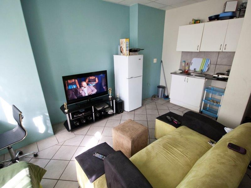 Compact open-plan living area featuring a kitchenette with built-in cabinetry, tiled flooring, and a functional layout suitable for apartment living.