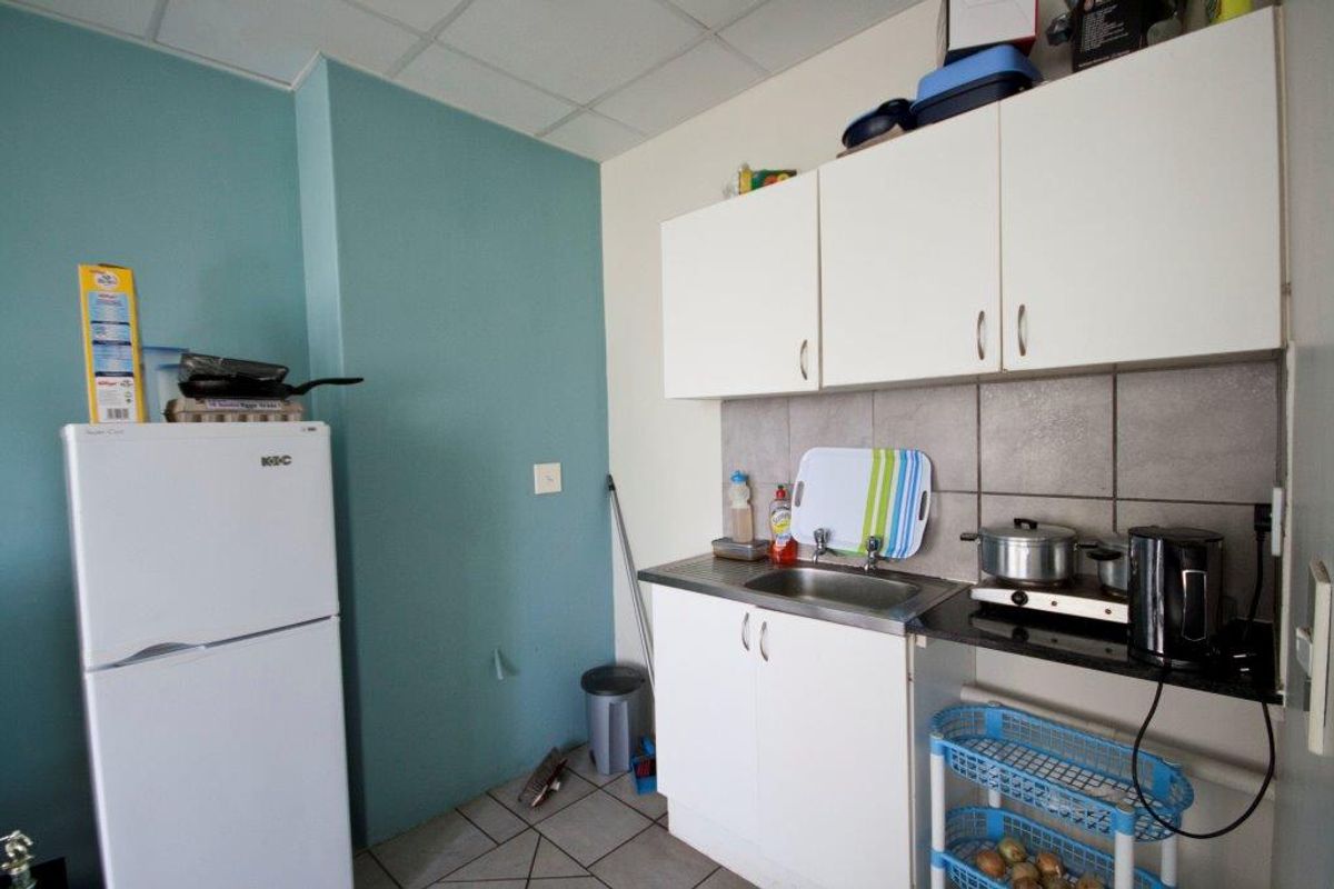 A compact kitchen area featuring basic white cabinetry, a stainless steel sink, tiled backsplash, and tiled flooring.