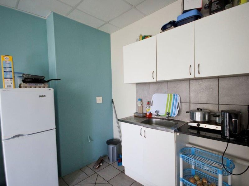 A compact kitchen area featuring basic white cabinetry, a stainless steel sink, tiled backsplash, and tiled flooring.