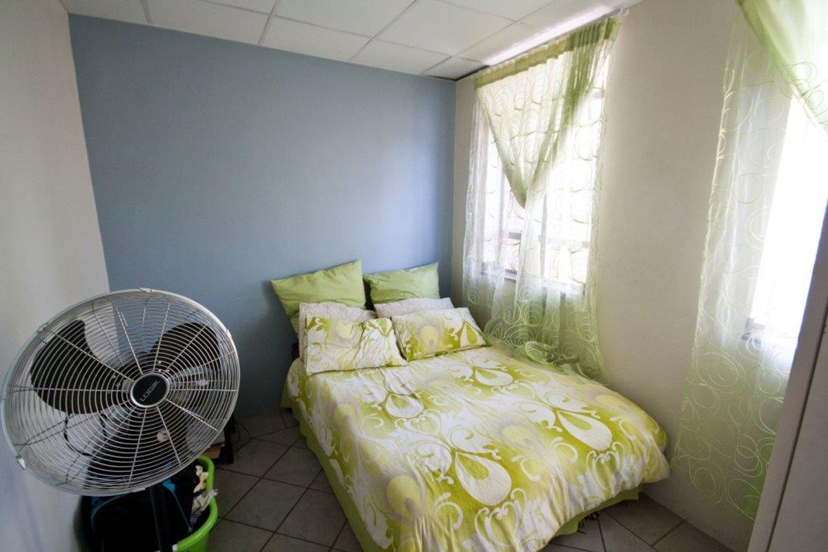 A compact bedroom featuring tiled flooring and a drop ceiling, providing a functional sleeping space.