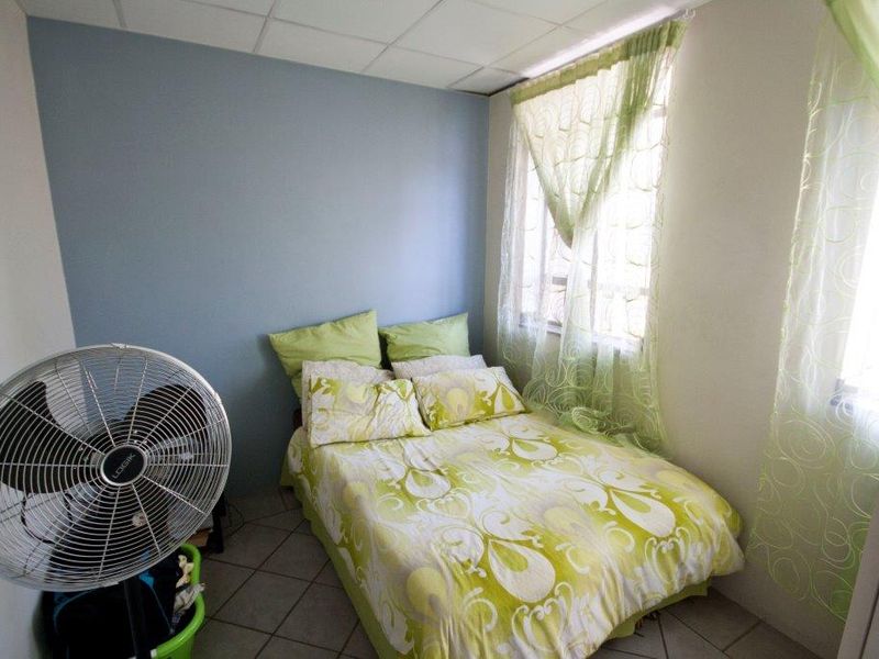 A compact bedroom featuring tiled flooring and a drop ceiling, providing a functional sleeping space.