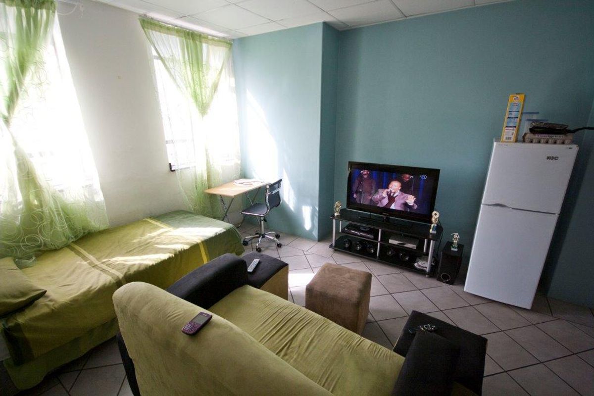 A compact open-plan living and sleeping area featuring tiled flooring and large windows, suitable for a studio apartment layout.