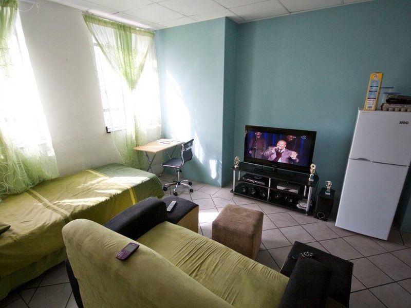 A compact open-plan living and sleeping area featuring tiled flooring and large windows, suitable for a studio apartment layout.