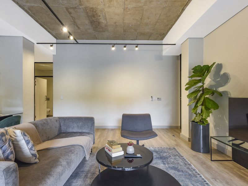 Modern living room featuring an exposed concrete ceiling, track lighting, and light wood-look laminate flooring in a contemporary apartment setting.