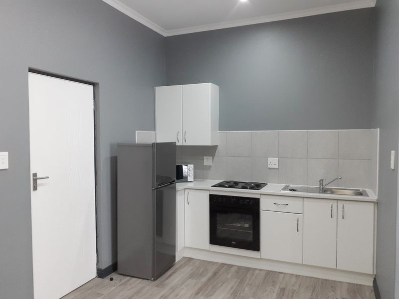 A clean, modern kitchen featuring white cabinetry, a built-in oven, hob, stainless steel sink, and neutral grey wall finishes.