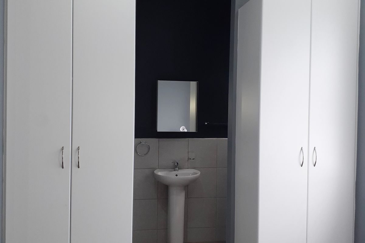 Bedroom featuring dual built-in wardrobes and an open-plan en-suite area with a pedestal basin and tiled splashback.