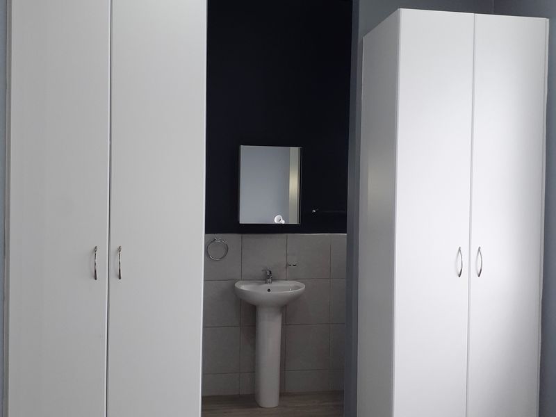 Bedroom featuring dual built-in wardrobes and an open-plan en-suite area with a pedestal basin and tiled splashback.