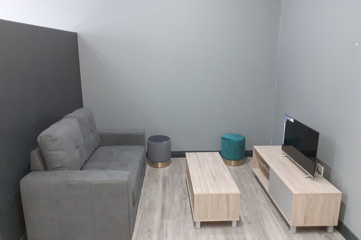 A compact living room area featuring light wood-look laminate flooring and neutral grey painted walls.