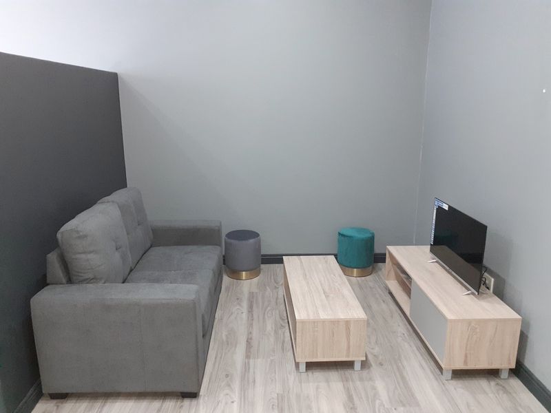 A compact living room area featuring light wood-look laminate flooring and neutral grey painted walls.