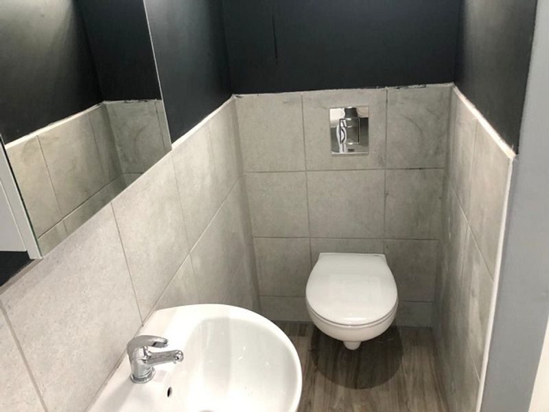 A compact guest bathroom featuring a wall-mounted toilet, chrome flush plate, and a pedestal basin with modern tiled finishes.