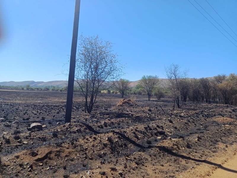 A view of the farm landscape showing open fields with visible signs of recent fire damage and utility infrastructure.