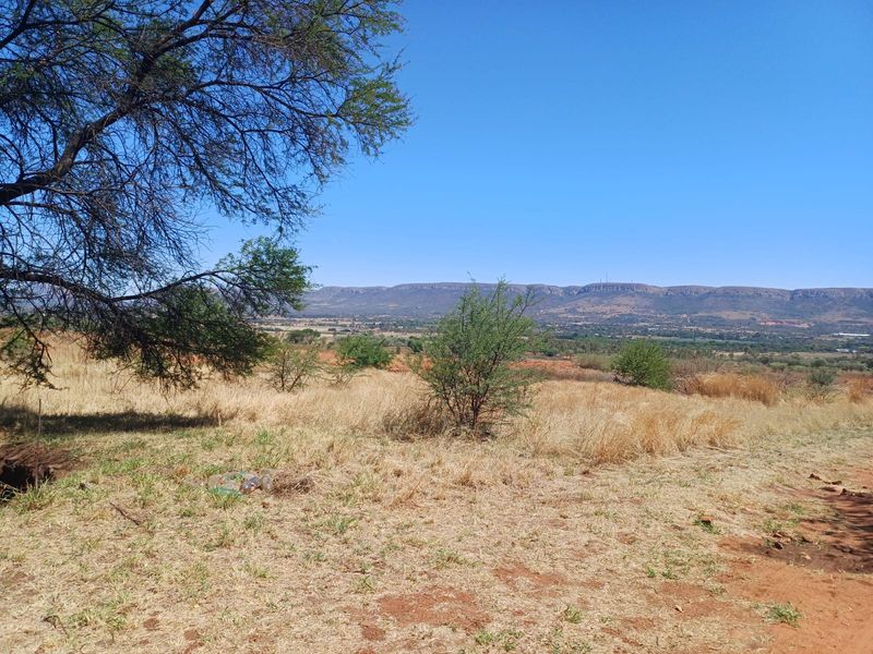 A scenic landscape view overlooking open farm fields and distant mountain ranges under a clear blue sky.
