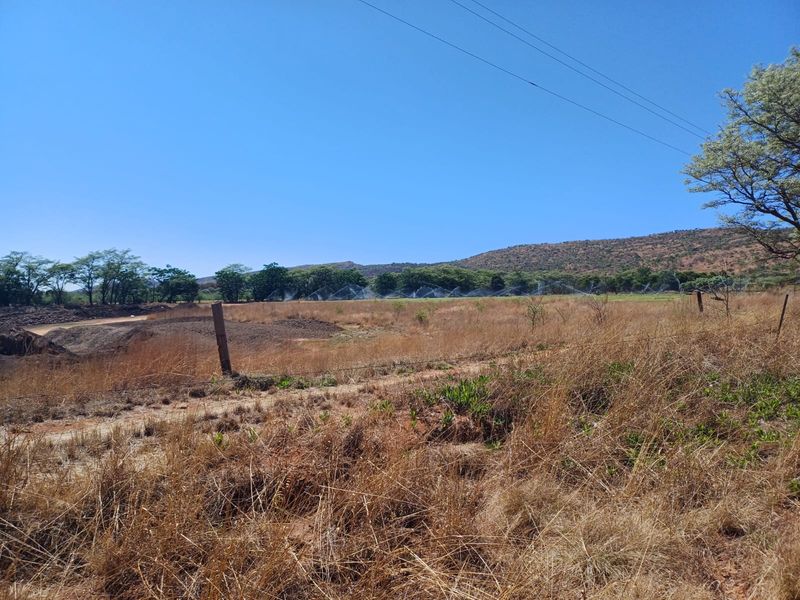 A wide landscape view of the farm property featuring dry grassland, wire fencing, and an active irrigation system in the distance.