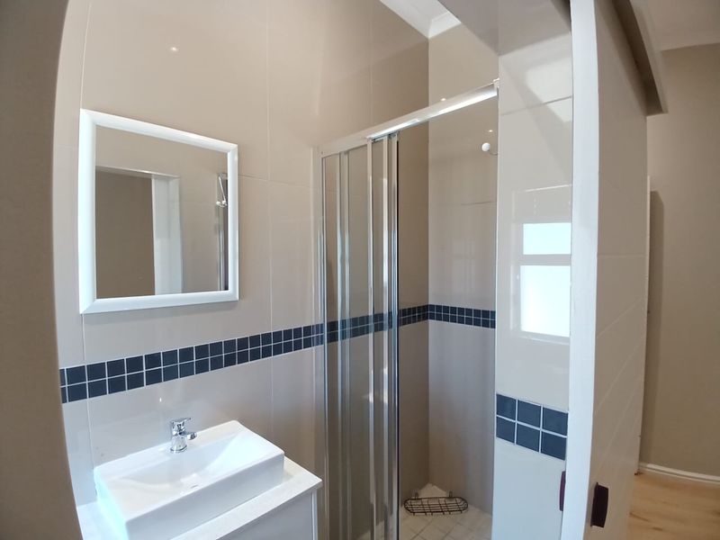 A clean, modern bathroom featuring a glass shower enclosure, a vanity basin with a mixer tap, and neutral wall tiling with a decorative border.