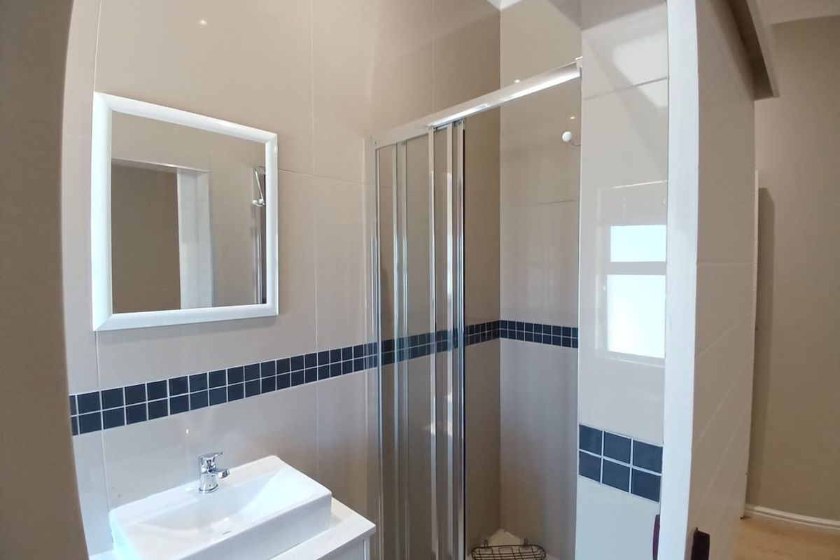 A clean, modern bathroom featuring a glass shower enclosure, a vanity basin with a mixer tap, and neutral wall tiling with a decorative border.