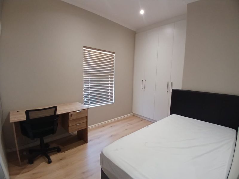 A well-maintained bedroom featuring light laminate flooring, neutral wall tones, built-in white cabinetry, and venetian blinds for privacy.
