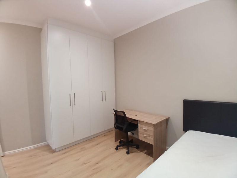 A clean, modern bedroom featuring light laminate flooring, neutral walls, and a large white built-in wardrobe with ample storage space.